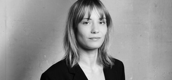 Rechtsanwältin Tanja Lucke steht entspannt vor einem hellen Hintergrund, mit dem Arm lässig auf der Lehne eines Sofas abgelegt, Schwarz-Weiß-Foto.